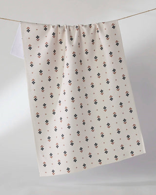 An off-white tea towel with a small geometric pattern, hanging from a thin wire against a neutral gray background.