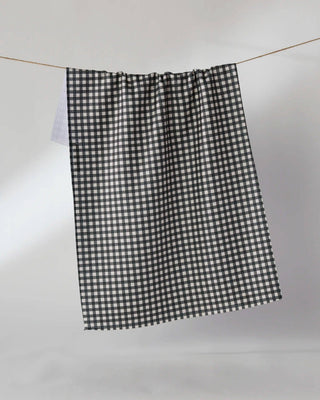 A black and white gingham checkered Geometry Tea Towel hanging from a thin wire rod against a plain light gray wall.