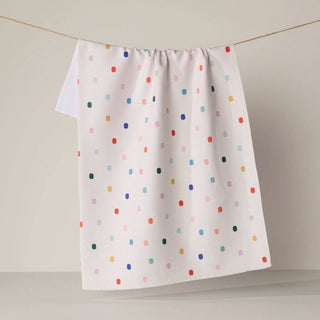 A white kitchen towel with a colorful polka dot pattern hanging from a thin wire against a neutral beige background.