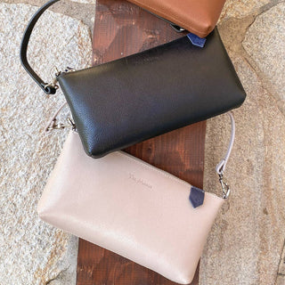 Two leather clutch bags, one in black and one in beige, displayed on a wooden surface.
Tin Marin