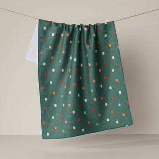 A green kitchen towel with a colorful polka dot pattern hanging from a string against a neutral beige background.