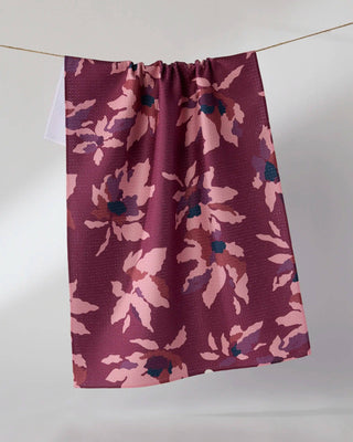 A Geometry Tea Towel hanging from a thin cord against a plain light gray wall. The curtain has a waffle texture and features a floral pattern in dusty pink, mauve, and dark navy blue.