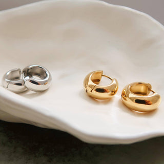 Pair of gold hoop earrings and siler hoop earrings on a white shell