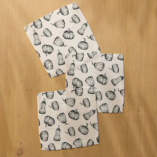 Three square dishclothes with a black and white pumpkin pattern, arranged on a light wood background.