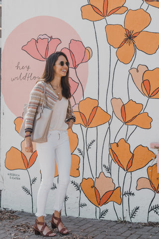 Woman standing in front of a floral mural with orange and pink flowers. Tote, leather tote
