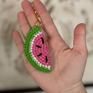 Hand holding a crocheted watermelon slice keychain with a blurred background