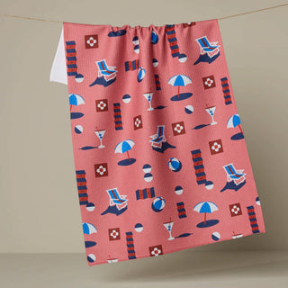 Red towel with beach-themed pattern hanging on a line against a beige background