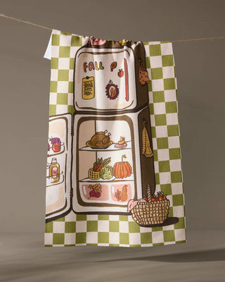 Checkered towel with fall-themed design of a refrigerator and harvest items on a gray background