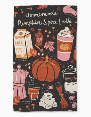 A rectangular kitchen towel with a black background printed with a colorful autumn-themed illustration of a pumpkin spice latte, including a pumpkin, coffee cup, milk carton, cinnamon stick, sugar jar, and handwritten text reading 'Homemade Pumpkin Spice Latte'.