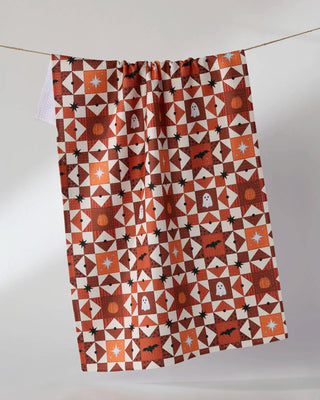 A tea towel with a Halloween-themed geometric pattern, hanging from a thin string against a plain light gray background.