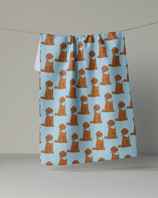 A light blue kitchen towel with an all-over repeating print of brown and white cartoon dogs, hanging from a string against a neutral gray background.