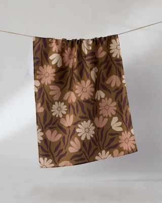 A Geometry Tea towel with a retro floral pattern in brown, beige, and pink, hanging from a thin wire against a plain light gray background.