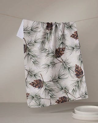 Towel with pine cone and branch pattern hanging on a line against a neutral background